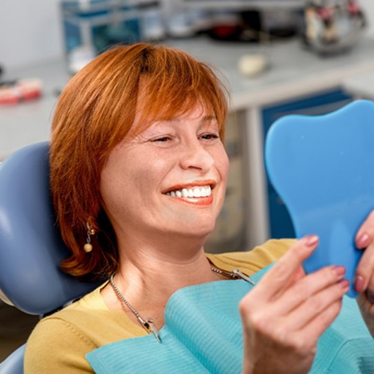 An older woman with red hair admiring her new and improved smile while at the dentist’s office