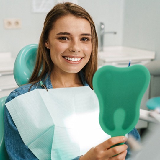 Woman in dental chair with hand mirror after getting dental implants in Shelton, CT