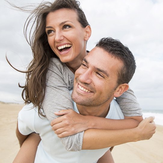 A younger couple on the beach and having fun while smiling after seeing a Cigna dentist in Shelton