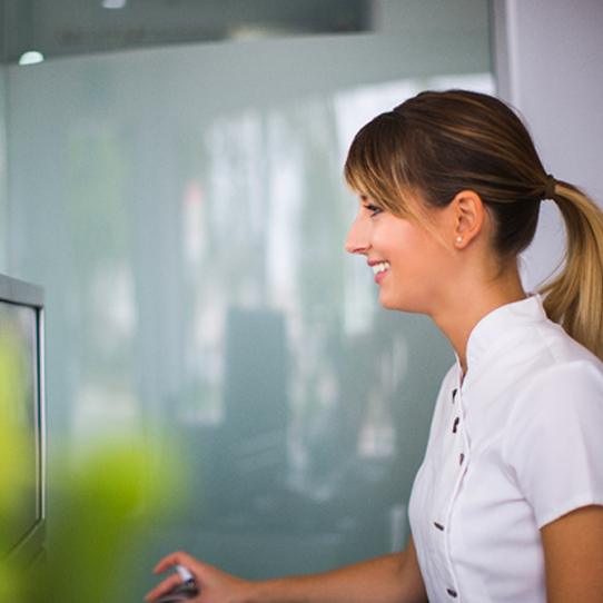 A dental receptionist smiling while seated behind a desktop computer