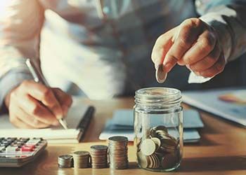 Person placing coin into jar while using a pen