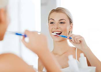 Woman brushing her teeth to prevent dental emergencies