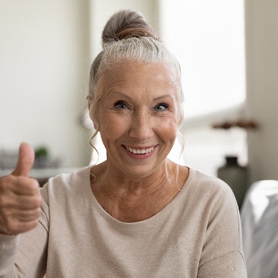 woman smiling and giving thumbs up after maintaining dental implants