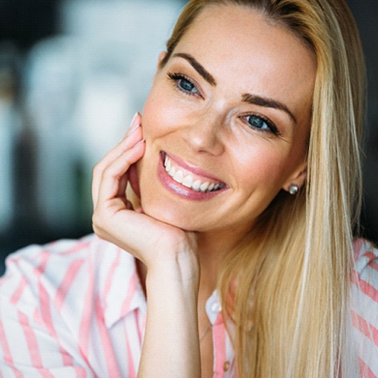 A young female with blonde hair propping her head on her hand and smiling after completing treatment with clear braces in Shelton