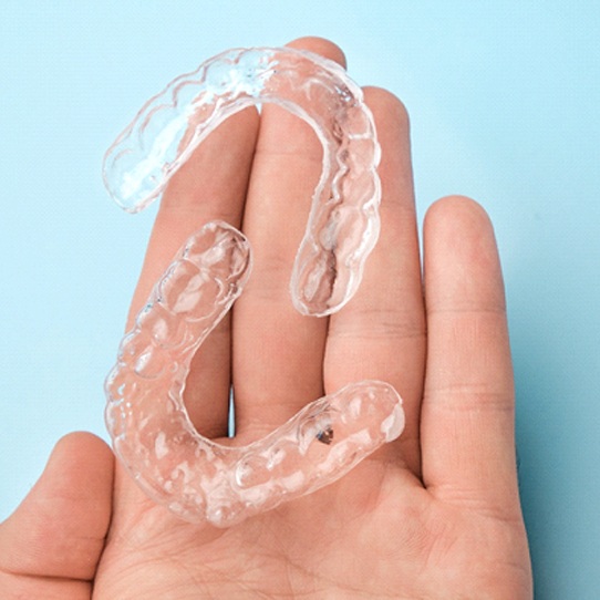 A hand holding upper and lower clear aligners designed to fit into a patient’s mouth