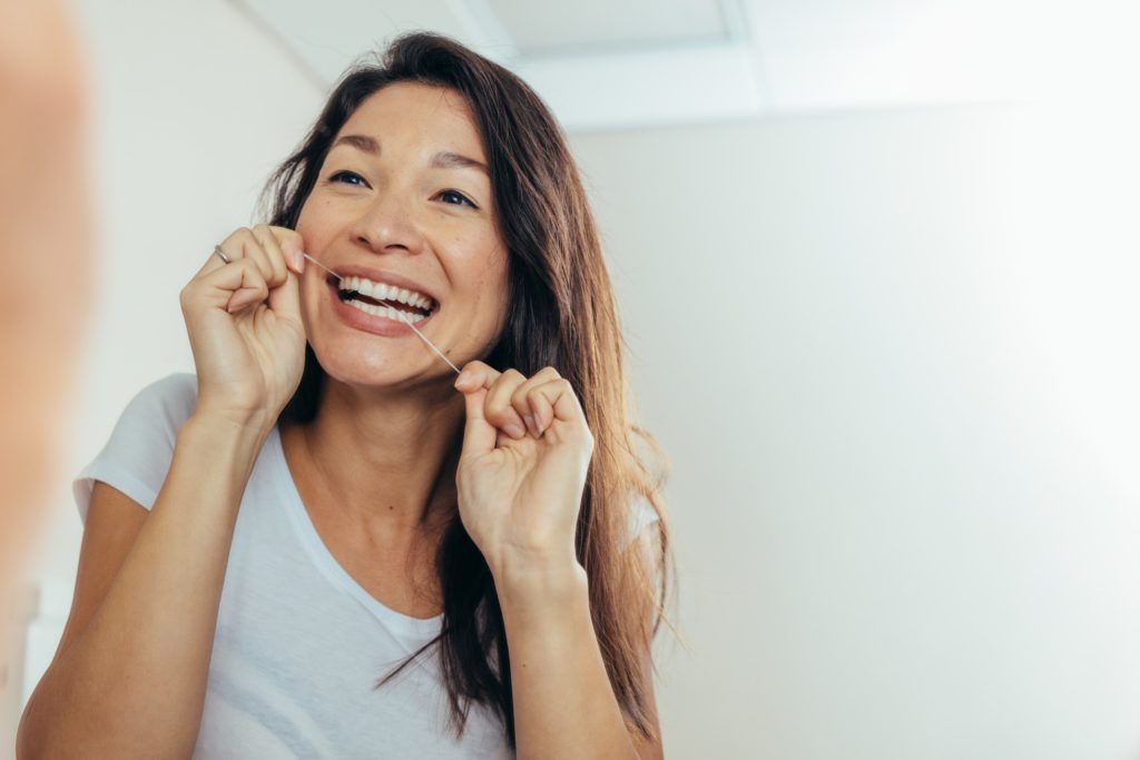 Woman smiling at reflection while flossing her teeth